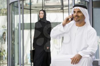 Royalty Free Photo of a Man With a Cellphone in a Lobby and a Woman Walking Behind