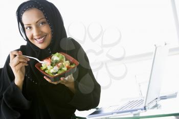 Royalty Free Photo of a Woman Wearing a Headset Eating a Salad at a Laptop