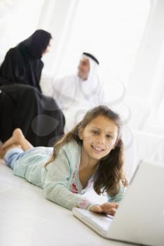Royalty Free Photo of a Child on the Floor With a Laptop With Her Parents Behind Her