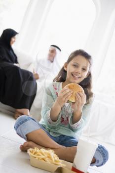 Royalty Free Photo of a Child Eating Fast Food With Her Parents Behind Her