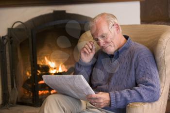 Royalty Free Photo of a Man Reading a Newspaper Beside a Fireplace