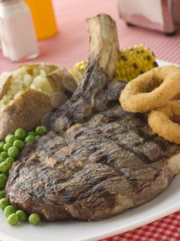 Royalty Free Photo of a Ribeye Steak on the Bone with Baked Potato, Peas, Onion Rings and Corn
