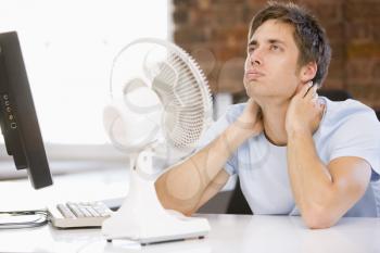 Royalty Free Photo of a Man Cooling Off With a Fan Beside a Laptop
