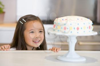 Royalty Free Photo of a Little Girl Looking at a Cake on the Counter