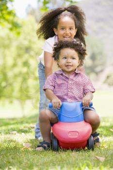 Royalty Free Photo of a Little Boy on a Riding Toy Getting a Push From His Sister
