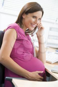 Royalty Free Photo of a Pregnant Woman at a Laptop Talking on a Telephone