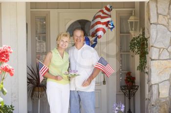 Royalty Free Photo of a Couple at the Front Door With a Plate of Cookies and Holding Flags