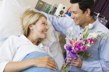 Royalty Free Photo of a Man Giving His Pregnant Wife Flowers in the Hospital