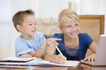Royalty Free Photo of a Girl Doing Homework and Her Brother Pointing at the Laptop
