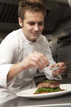 Chef Adding Seasoning To Dish In Restaurant Kitchen