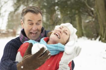 Senior Couple Having Snowball Fight In Snowy Woodland