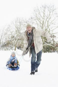 Father Pulling Son On Sledge Through Snowy Landscape