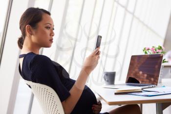 Pregnant Businesswoman Reading Text Message In Office