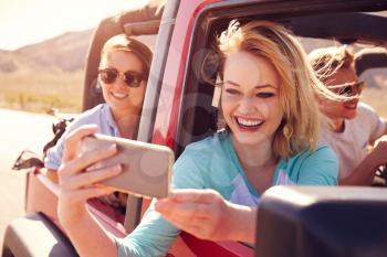 Friends On Road Trip In Convertible Car Taking Selfie