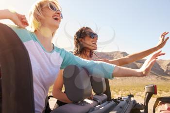 Two Female Friends On Road Trip In Back Of Convertible Car