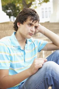 Unhappy Male Teenage Student Sitting Outside On College Steps