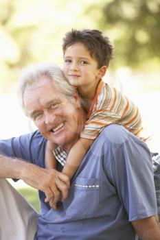 Grandfather Giving Grandson Ride On Back In Park