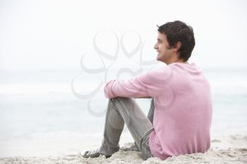 Young Man On Holiday Sitting On Winter Beach