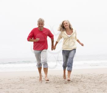 Senior Couple On Holiday Running Along Winter Beach
