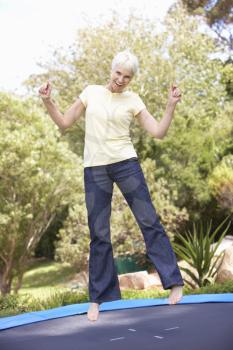 Senior Woman Jumping On Trampoline In Garden