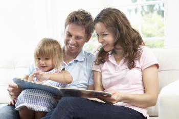 Family Sitting On Sofa Reading Book At Home
