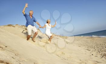 Senior Couple Enjoying Beach Holiday Running Down Dune