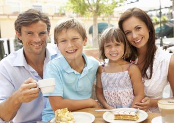 Young Family Enjoying Cup Of Coffee And Cake In Caf Together