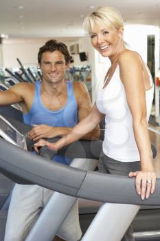 Senior Woman Working With Personal Trainer On Running Machine In Gym