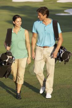 Couple Walking Along Golf Course Carrying Bags