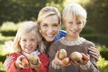 Young mother and children in garden pose with vegetables