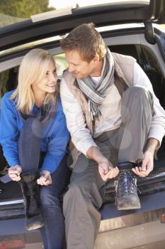 Young couple tie boots at rear of car