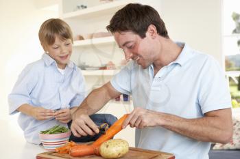 Happy young man with boy peeling vegetables in kitchen