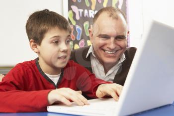 Schoolboy In IT Class Using Computer With Teacher