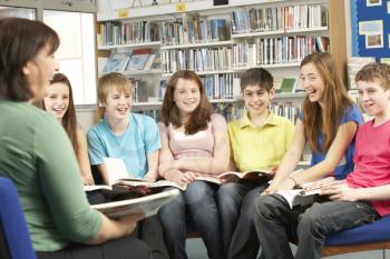 Teenage Students In Library Reading Books With Tutor