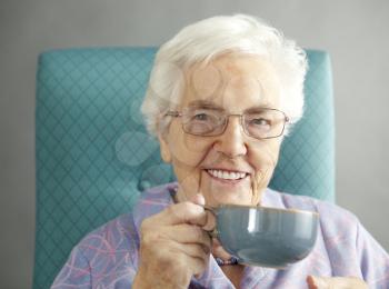 Senior Woman Relaxing In Chair With Hot Drink