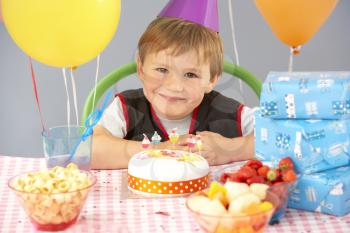 Young boy with birthday cake and gifts at party