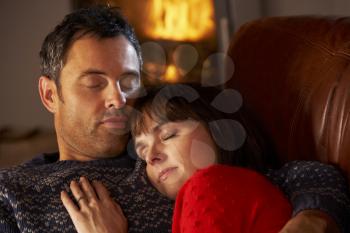 Middle Aged Couple Cuddling On Sofa By Cosy Log Fire