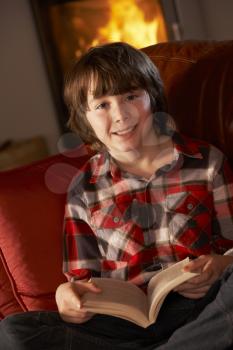 Young Boy Relaxing With Book By Cosy Log Fire