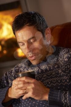 Middle Aged Man Relaxing With Hot Drink By Cosy Log Fire