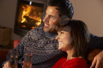 Middle Aged Couple Sitting Sofa By Cosy Log Fire With Glass Of Champagne