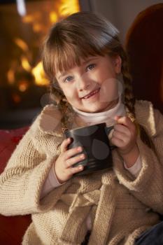 Young Girl Relaxing With Hot Drink By Cosy Log Fire