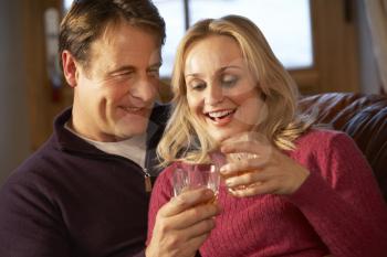 Middle Aged Couple Sitting On Sofa With Glasses Of Whisky