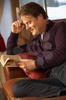 Middle Aged Man Relaxing With Book Sitting On Sofa