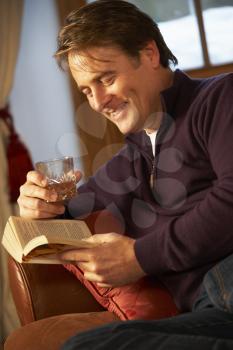 Middle Aged Man Relaxing With Book Sitting On Sofa Drinking Whisky