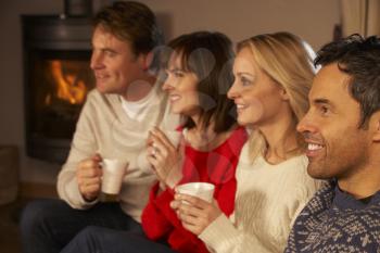 Group Of Middle Aged Couples Sitting On Sofa With Hot Drinks Watching TV