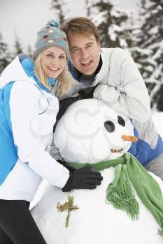 Middle Aged Couple Building Snowman On Ski Holiday In Mountains
