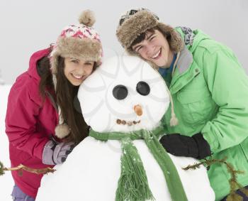 Two Teenagers Building Snowman On Ski Holiday In Mountains