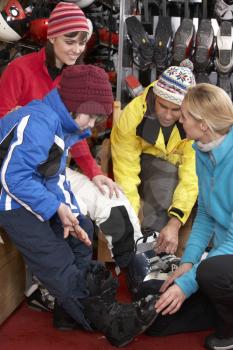 Sales Assistant Helping Family To Try On Ski Boots In Hire Shop