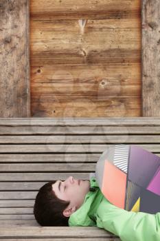 Teenage Boy With Snowboard On Ski Holiday Lying On Wooden Bench
