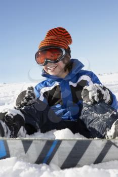 Young Boy Sitting In Snow With Snowboard